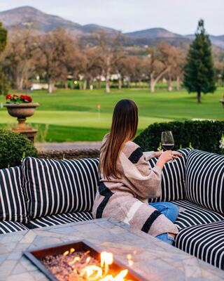 Girl by fire pit overlooking Golf Course with glass of wine in hand