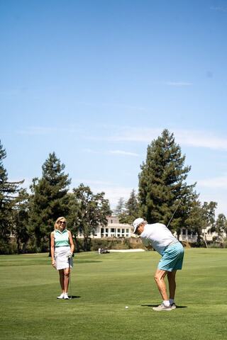 Man golfing at tee while woman golfer looks on.