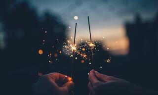 two hands holding sparklers at sunset