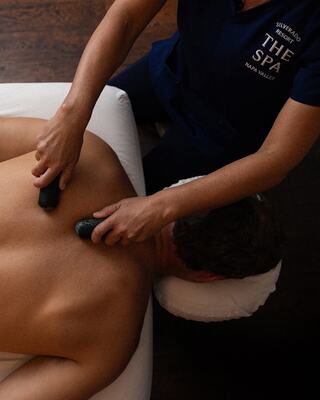 A therapist applies heated stones on a person's back during a relaxing spa treatment. The setting is serene and focused on wellness.