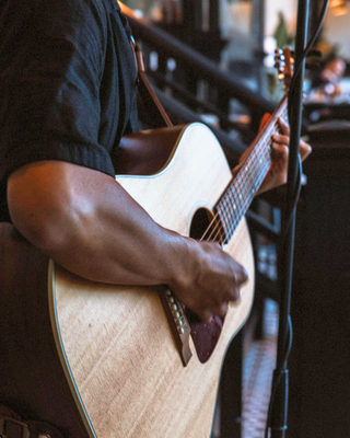 A person strums an acoustic guitar, showcasing their hand technique, while a vibrant setting buzzes in the background.
