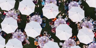 Aerial view of numerous tables covered with umbrellas, filled with people enjoying a vibrant outdoor gathering.