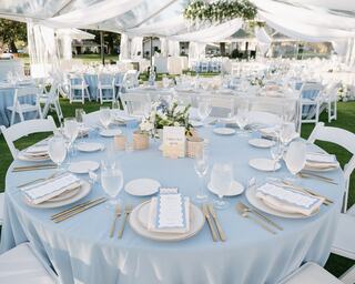 A beautifully set table with light blue linens, elegant tableware, and floral centerpieces, surrounded by a festive outdoor setting.
