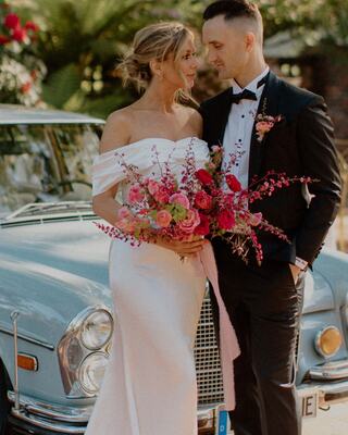 Bride and groom embracing each other in front of a vintage car in an outdoor setting