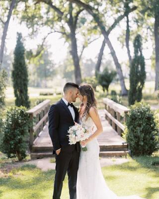 Bride and groom in front of a wooden bridge in an outdoor nature setting surrounded by trees, and grass