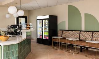 A modern café interior featuring a sleek counter, comfortable seating, a display fridge, and stylish decorative elements in soft colors.