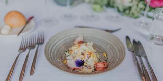 Fancy plated food topped with flowers on a table with silverware