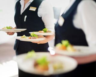 Torso of two food servers holding plates of food