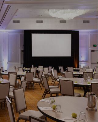 Room set up for a group of people with round tables and chairs and a projector screen