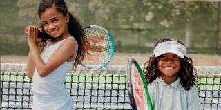 Two Young Siblings Holding Tennis Racquets on a Tennis Court