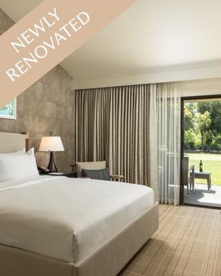A Hotel Suite Bedroom with art on the wall, side table and a upholstered chair