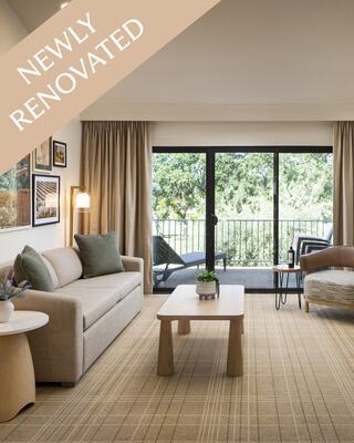 A Modern and Classy Hotel Suite Living Room with a Chandelier, Furniture, Fireplace, TV, Flowers and a Bottle of Wine with Wineglasses, and a View of the Outdoor Patio