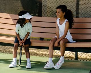 Two young children sitting on a bench holding pickleball racquets