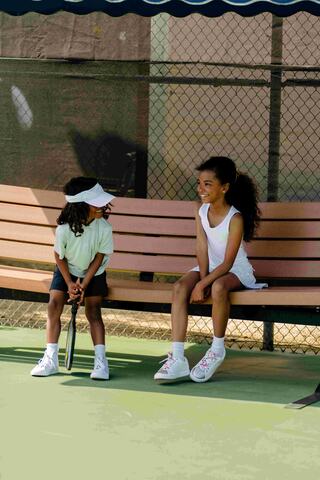 Two young children sitting on a bench holding pickleball racquets