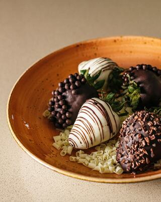 A Bowl of Specialty Chocolate-Covered Strawberries with Different Types of Chocolate on Top of Chocolate Shavings