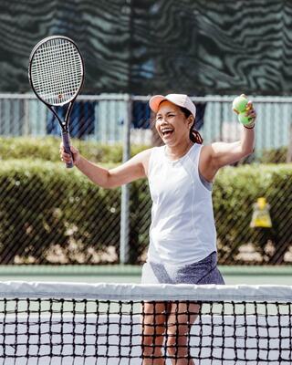 A Happy Woman Playing Tennis Holding a Racquet and Tennis Ball on the Court