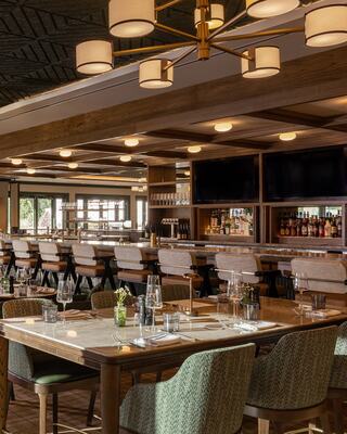 A modern restaurant features elegant wooden decor, a spacious bar, plush seating, and a warm ambiance, perfect for dining and gatherings.