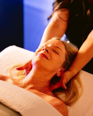 A woman relaxes with her eyes closed as a therapist provides a soothing neck massage in a tranquil setting.