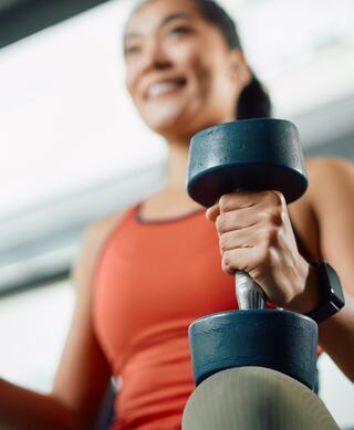 A person holds a dumbbell in a bright gym, smiling confidently while engaged in a workout, showcasing fitness and determination.