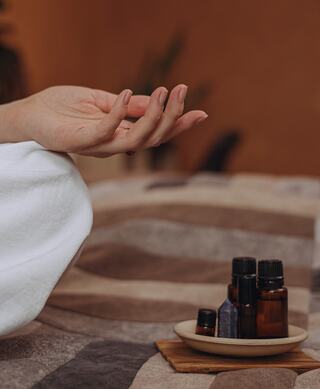 A relaxed hand rests above a tray of essential oil bottles on a cozy, patterned blanket, evoking tranquility and wellness.