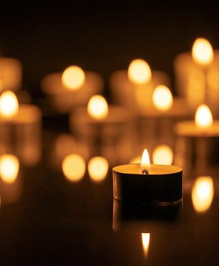 Warm candlelight flickers softly against a dark background, creating a serene and cozy atmosphere with reflections glimmering nearby.