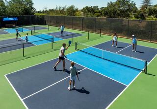 A vibrant outdoor tennis facility with multiple courts, where players of various ages are engaged in games and practice sessions.