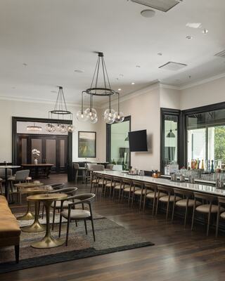 A stylish, contemporary bar area featuring elegant lighting, wooden floors, and a long counter with seating, creating a welcoming atmosphere.