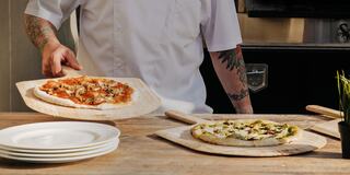 Chef with Arm Tattoos Putting a Wood Fired Pizza on a Table