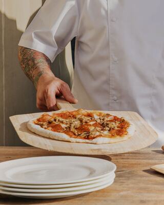 Chef with Arm Tattoos Putting a Wood Fired Pizza on a Table