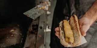 Hand Holding Burderdog with Melted Cheese Over Grill