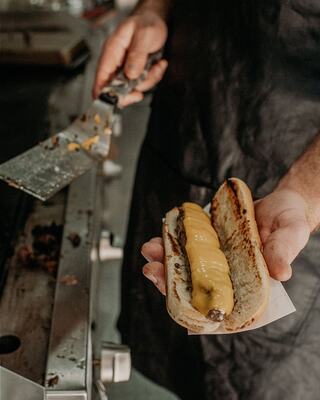 Hand Holding Burderdog with Melted Cheese Over Grill