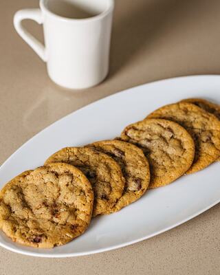 A Plate of Large Fresh-Baked Chocolate Chip Cookies Next to a Ceramic Mug for Milk