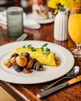 Breakfast Food Plated on a Dining Table at a Restaurant with Silverware, Beverages, and Flowers in a Vase