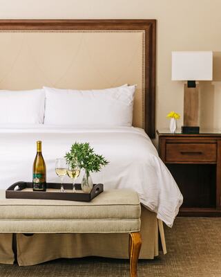 White bed and bench at the foot of the best with wine on tray