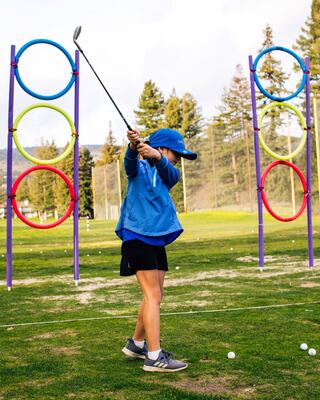 Young Boy in a Blue Shirt Taking a Swing at a Golf Ball on the Golf Course