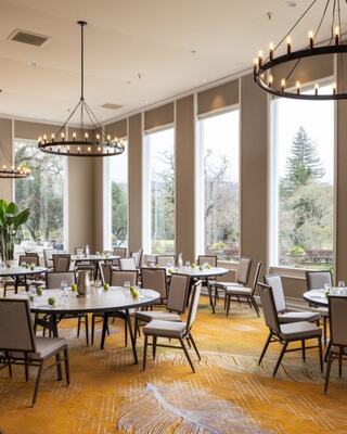 A Meeting Room with a Dining Table, Chairs, and a Fireplace with a Mounted Mirror and Flowers in Vases
