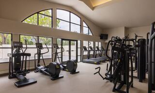 A modern gym area features various exercise machines, large windows providing natural light, and a spacious, inviting atmosphere.