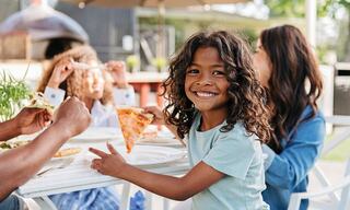 Young Boy Eating Pizza Outdoors with His Family