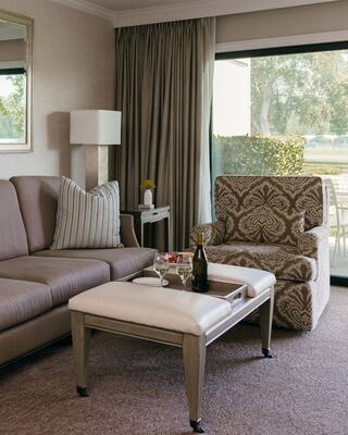 A Hotel Suite Living Room with Furniture, A Bottle of Wine and Vase of Flowers, and Outdoor Patio View