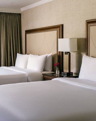 A Modern Hotel Room with Two Beds, a Lamp, and a Vase with Flowers in it in Napa