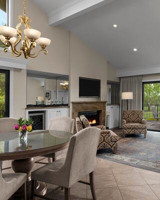 A Modern and Classy Hotel Suite Living Room with a Chandelier, Furniture, Fireplace, TV, Flowers and a Bottle of Wine with Wineglasses, and a View of the Outdoor Patio