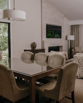 A Living Room in a Hotel Suite with Dining Furniture, a Mounted TV, Lamps, a Decorative Vase, and Door to an Outdoor Patio